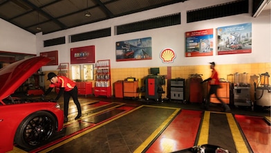 A red Ferrari sitting on a Shell station forecourt with a man leaning on a petrol pump